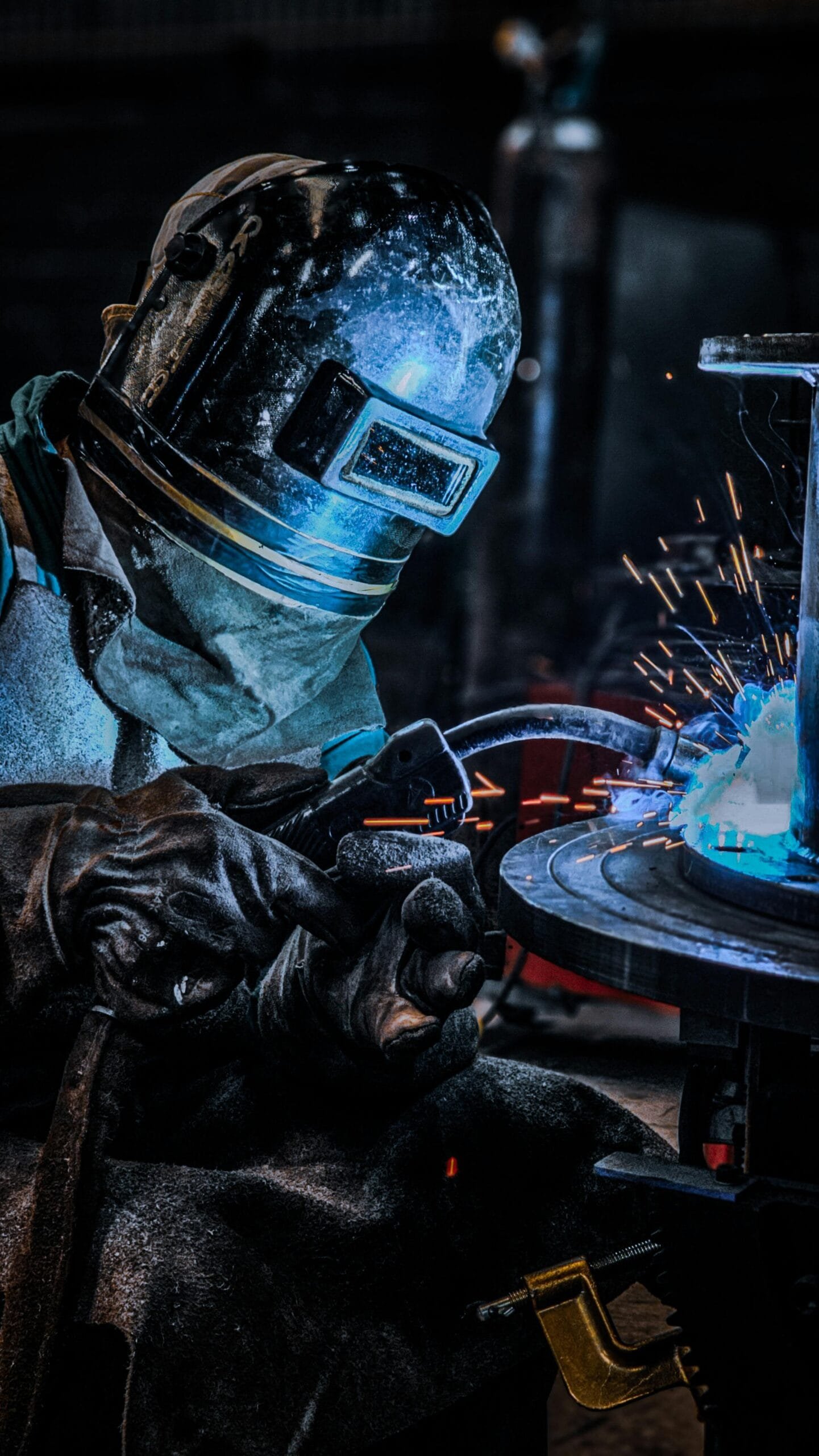 A welder with protective gear works on metal, emitting bright sparks in an industrial setting.